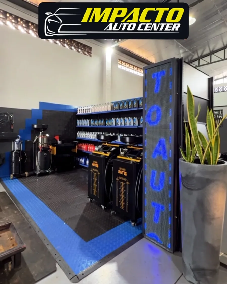 Interior da oficina Impacto Auto Center com a placa luminosa e a prateleira de óleos